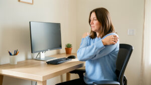 Une femme effectue des mouvements doux des épaules près d’un poste informatique réglé de manière ergonomique.