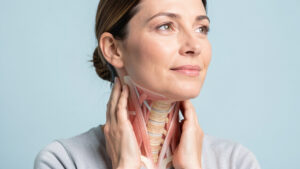 Femme touchant doucement sa nuque avec une représentation anatomique discrète de la colonne cervicale.