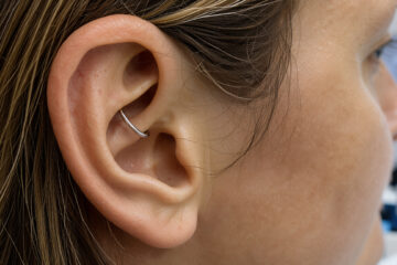 Gros plan réaliste de l’oreille d’une femme portant un discret piercing daith, dans une ambiance clinique évoquant une réflexion sur le soulagement de la migraine.